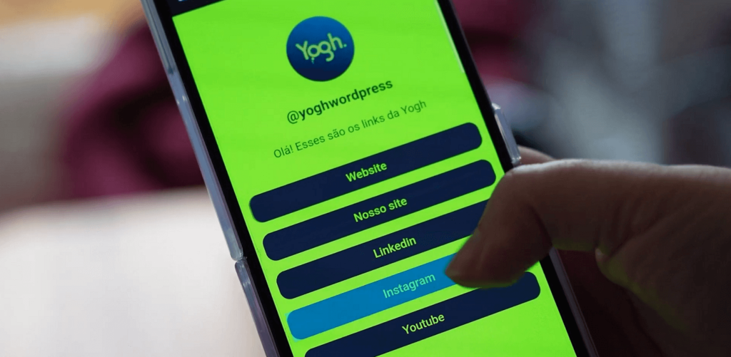 Mão de uma pessoa segurando um celular com a tela mostrando a página de links da Yogh feita com o plugin Yogh Bio Links